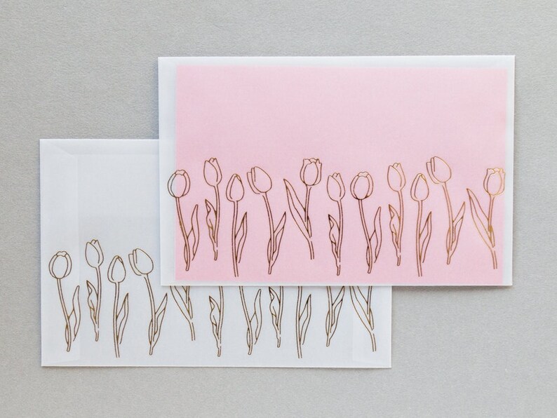 Puede incluir: Dos sobres blancos con un sobre rosa en la parte superior. Los sobres tienen un dise&ntilde;o de tulipanes en pan de oro a lo largo del borde inferior.