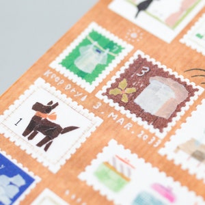 May include: A sheet of decorative washi tape featuring various illustrations, including a dog, a shirt, a flower, and a building. The tape is printed on a brown background with white borders and includes handwritten text such as "Keep Dry" and "3 Mar. 2013".