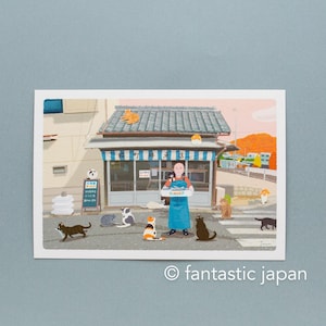 May include: A postcard with an illustration of a shop with a blue and white striped awning, surrounded by cats. A person in a blue apron holds a box. The text "fantastic japan" is at the bottom of the image.
