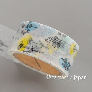 Puede incluir: Un rollo de cinta washi blanca con un dise&ntilde;o floral. La cinta presenta contornos negros de flores y hojas con acentos azul y amarillo como de acuarela. La cinta est&aacute; en un carrete de cart&oacute;n marr&oacute;n.