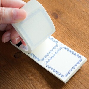 Puede incluir: Un rollo de cinta washi decorativa con un dise&ntilde;o de borde azul y blanco. La cinta se est&aacute; desenrollando para revelar una hoja de papel blanco con dos marcos de borde azul y blanco.