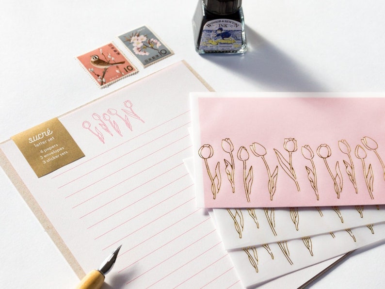 Puede incluir: Un juego de seis papeles de carta y sobres con un dise&ntilde;o de tulip&aacute;n dorado. El papel tiene l&iacute;neas rosas y los sobres son rosas. El juego tambi&eacute;n incluye tres juegos de pegatinas. Los juegos de pegatinas no son visibles en la imagen.