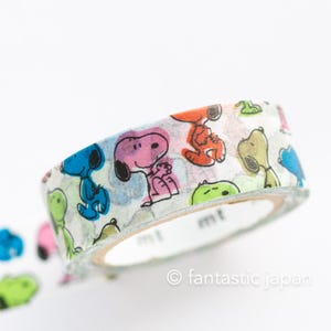 May include: A roll of white washi tape with a colourful pattern of Snoopy characters. The tape is partially unrolled, revealing the design. The tape is labelled "mt".