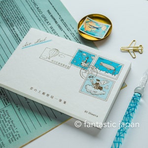 Puede incluir: Un bloc de notas blanco con un diseño azul y blanco de sellos que representan un globo aerostático, un hombre pescando, un dirigible y un hombre con alas. El bloc de notas tiene el texto "雲の上郵便局一筆箋" (que significa "Oficina de correos en la nube - Una carta") y "80 Hojas" impreso en él.