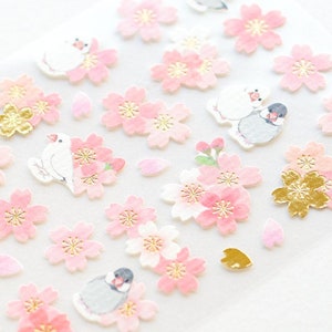Könnte beinhalten: Rosa und goldene Blumenaufkleber mit kleinen Vogelillustrationen. Die Aufkleber zeigen verschiedene Kirschblütenmotive mit goldenen Akzenten.