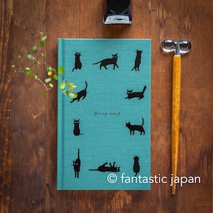 May include: A teal fabric-covered diary with the text Diary 2017 printed in the centre. The cover features various black cat silhouettes in different poses. Beside the diary is a wooden dip pen with a clear glass nib and an ink bottle.