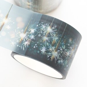 May include: A roll of decorative washi tape featuring a dark background with white and light blue starburst-like designs. The tape has a white interior and is partially unrolled, revealing the design.