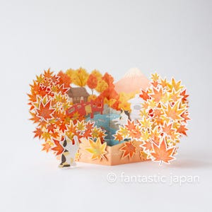 May include: A pop-up card featuring a Japanese autumn scene with orange and yellow maple leaves, a red bridge, and a mountain. A small cat figure is included. The text "fantastic japan" is at the bottom.