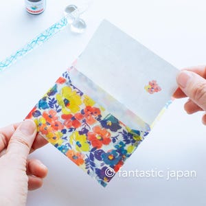 May include: A floral patterned stationery set featuring a colorful envelope and matching lined stationery. The envelope displays a vibrant pattern of yellow, red, and blue flowers. The stationery set is held open, revealing the blank, lined paper.