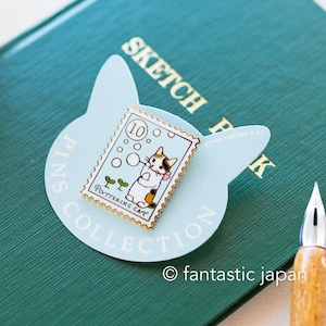 May include: A cat-themed enamel pin in the shape of a postage stamp, featuring a cartoon cat blowing bubbles. The pin is light blue with gold trim and the text "Pottering Cat". The pin is on a light blue cat-shaped card.