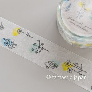 Puede incluir: Un rollo de cinta washi con un dise&ntilde;o floral. La cinta presenta delicados dibujos de l&iacute;nea negra de flores y hojas con lavados de acuarela en tonos azules, verdes y amarillos. El texto "Botanical garden" y "Hutte Paper Works" est&aacute; impreso en la cinta.