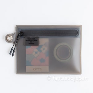 May include: A clear grey zippered pouch with a black zipper and a black label that says "QUICK COLOR" and "THE PERFECT COLOR PARTNER" with a small black label that says "KITTA" inside the pouch. There is a roll of washi tape and a patterned card inside the pouch.