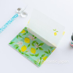 May include: An open stationery set featuring a lemon design. The set includes a notepad with lined pages and a matching envelope, decorated with yellow lemons, white blossoms, and green leaves on a light green background. A glass pen with blue accents is visible.