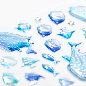 May include: A collection of blue and white glass sea life ornaments, including a whale shark, a manta ray, and various fish. The ornaments are iridescent and have a 3D effect.