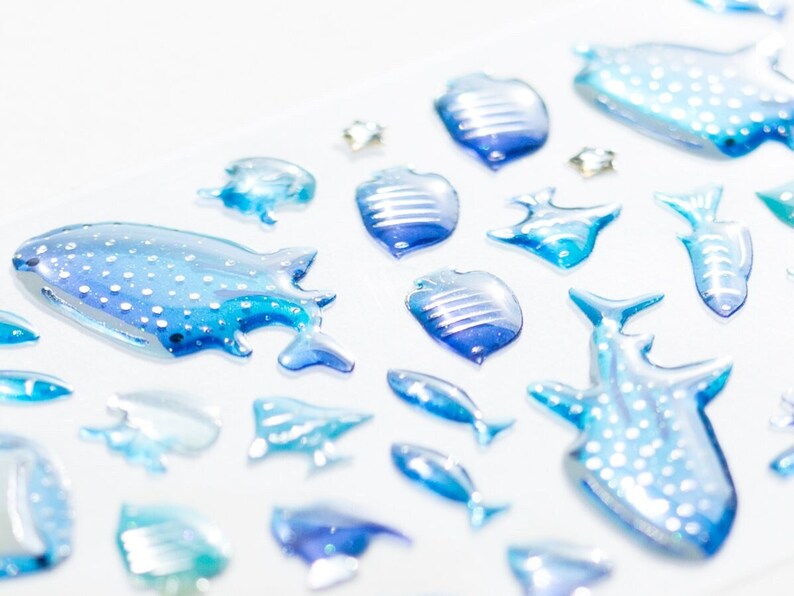 May include: A collection of blue and white glass sea life ornaments, including a whale shark, a manta ray, and various fish. The ornaments are iridescent and have a 3D effect.