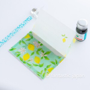 May include: A stationery set featuring a lemon theme. The set includes a notepad with lined pages and a lemon illustration, a glass pen with a blue design, and a bottle of ink. The notepad has a lemon and floral pattern on the cover.