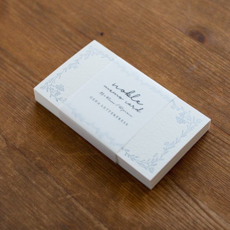 May include: A stack of white memo cards with a blue floral border and the text "noble memo card 85 x 47mm / 40 piece OEDA LETTERPRESS" printed on the front.