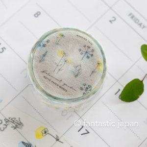 Puede incluir: Un rollo de cinta washi con un dise&ntilde;o floral. La cinta es blanca con un fondo acuarela azul claro y presenta delicados dibujos en negro de flores y plantas. El texto "Botanical garden" y "H&Uuml;TTE PAPER WORKS" est&aacute; impreso en la cinta.