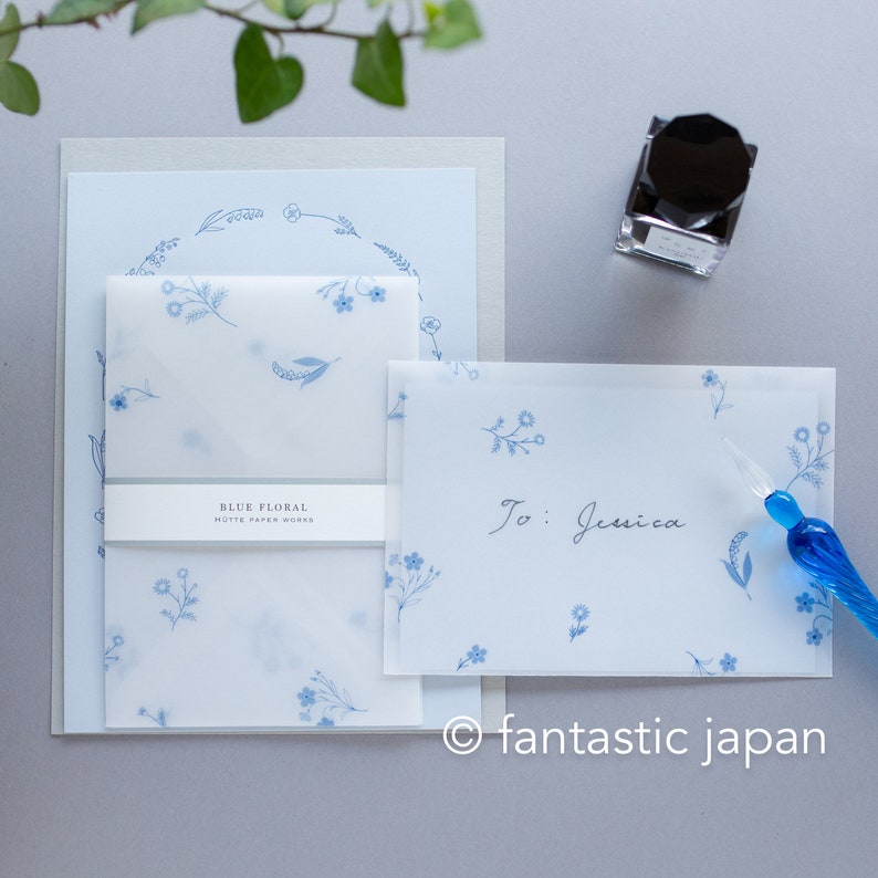 Pode incluir: Conjunto de papelaria com desenhos florais azuis. Inclui um cart&atilde;o, um envelope e papel de carta, todos decorados com uma coroa floral e flores espalhadas. Uma caneta de vidro e um frasco de tinta tamb&eacute;m est&atilde;o presentes. O cart&atilde;o tem a inscri&ccedil;&atilde;o "To: Jessica".