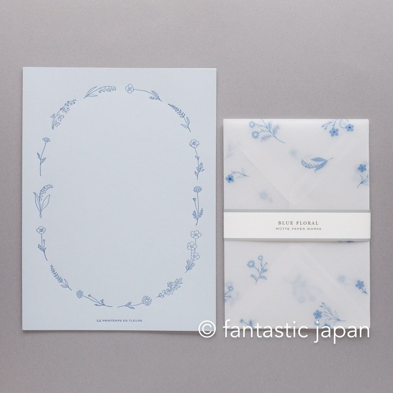 Pode incluir: Um conjunto de papelaria azul claro com um design floral. O conjunto inclui uma folha grande de papel com uma borda floral azul e um envelope correspondente com um padr&atilde;o floral. O texto "BLUE FLORAL" e "HUTTE PAPER WORKS" s&atilde;o vis&iacute;veis.