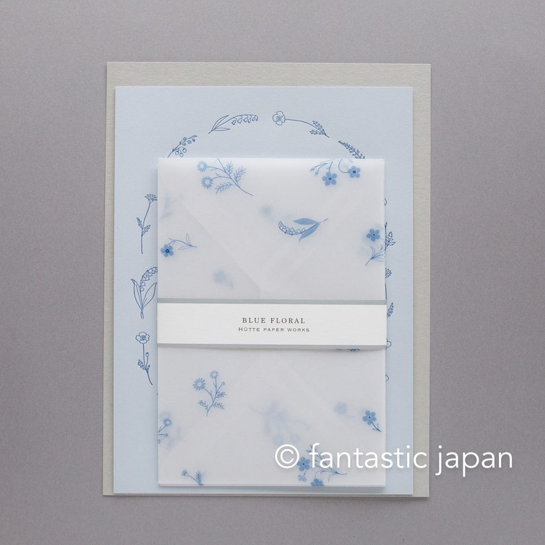 Pode incluir: Um conjunto de papelaria com fundo azul claro e um design de coroa de flores. O conjunto inclui um envelope e papel de carta azul claro com um delicado padr&atilde;o floral azul. O texto "BLUE FLORAL HOTTE PAPER WORKS" &eacute; exibido em um r&oacute;tulo branco.