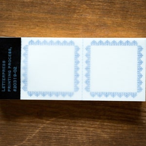 Puede incluir: Dos etiquetas blancas en blanco con bordes decorativos azules. Las etiquetas est&aacute;n unidas a un fondo negro con el texto "LETTERPRESS PRINTING PROCESS #20319-02".