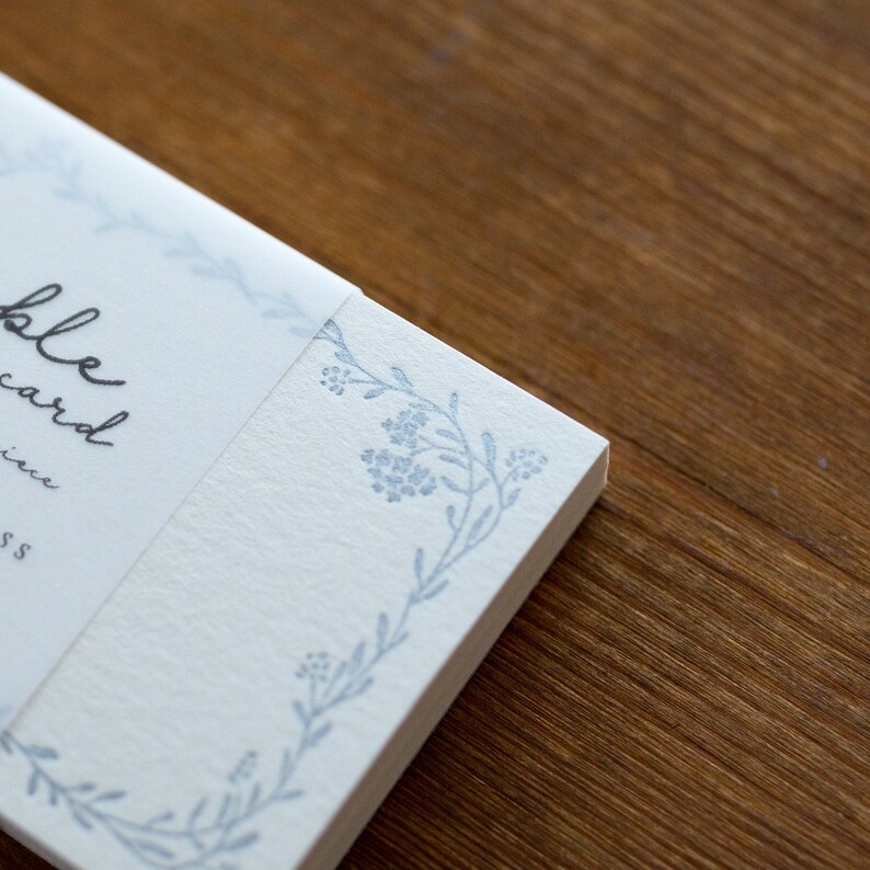 May include: A stack of white note cards with a blue floral design on the edge. The text "remarkable card" is printed on the front of the cards.