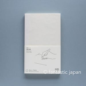 May include: A white MD Notebook B6 Slim Blank with a paper belly band. The band features a black line drawing of a hand writing with a pen, along with the text MD Notebook, B6 Slim Blank, and the phrase Painting moves you forward.