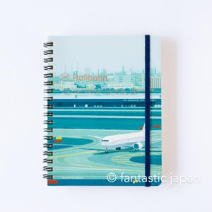 May include: Spiral-bound notebook with a cover featuring an illustration of an airplane on a runway. The notebook has a blue elastic band and the text "Rollbahn" is visible on the top. The bottom right corner has the text "fantastic japan".