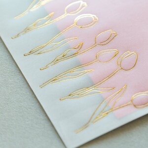 Puede incluir: Una hoja de papel blanco con un borde rosa. El papel est&aacute; decorado con tulipes de l&aacute;mina dorada.