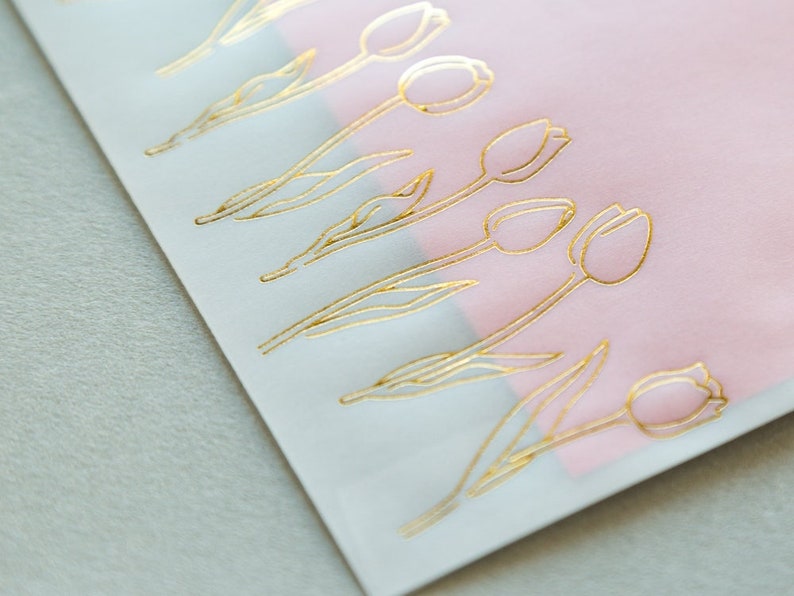 Puede incluir: Una hoja de papel blanco con un borde rosa. El papel est&aacute; decorado con tulipes de l&aacute;mina dorada.