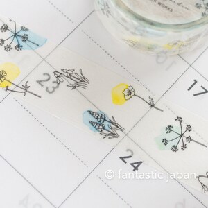 Puede incluir: Un rollo de cinta washi transparente con un dise&ntilde;o floral. La cinta presenta flores y hojas amarillas y azules en acuarela, con contornos negros. La cinta est&aacute; parcialmente desenrollada y se encuentra en una p&aacute;gina de calendario con los n&uacute;meros 23, 24 y 17 visibles. El texto "fantastic japan" tambi&eacute;n es visible en la p&aacute;gina del calendario.