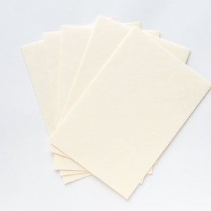 Puede incluir: Una pila de cinco hojas de papel rectangulares, de color blanco roto, en blanco.