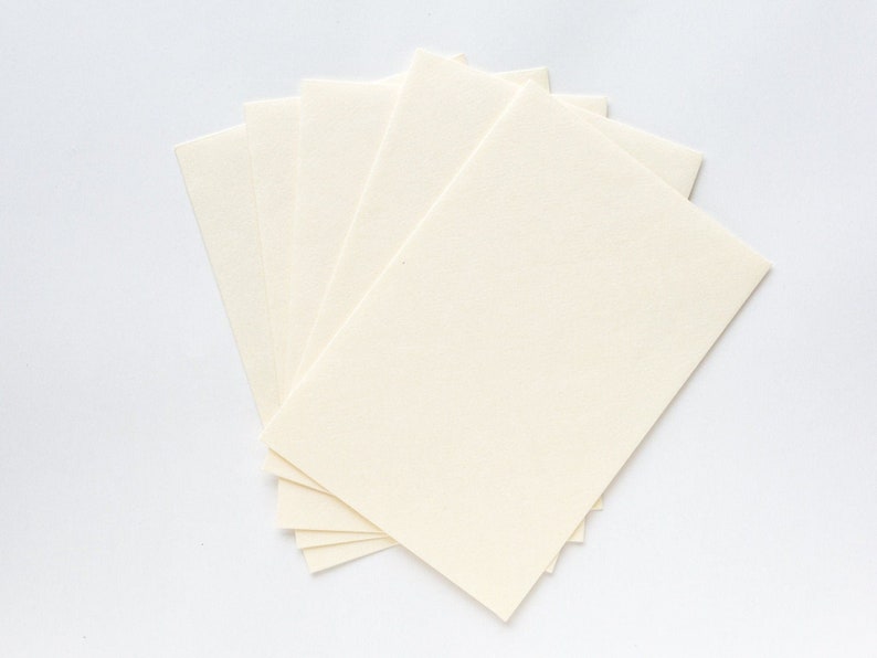 Puede incluir: Una pila de cinco hojas de papel rectangulares, de color blanco roto, en blanco.