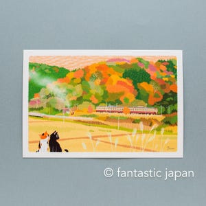 Peut inclure: Une carte postale représentant un paysage d'automne coloré avec un train et deux chats. La scène comprend un champ, des arbres aux teintes orange, rouge et verte, et un train. Le texte "fantastic japan" est en bas.