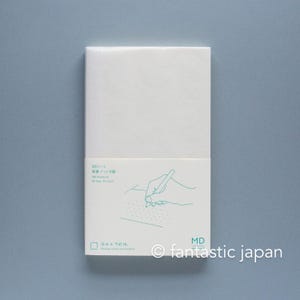 以下が含まれることがあります： 白いMDノートで、ティール色のテキストとドット方眼に書き込む手の線画が描かれた紙帯が付いています。テキストにはMDノート、新書ドット方眼、MD Notebook、そしてFreeing notes you forwardというフレーズが記載されています。