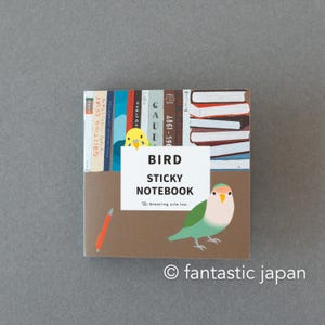 Może przedstawiać: Kwadratowy notatnik samoprzylepny z motywem ptaków. Okładka przedstawia kolorową ilustrację ptaka, książek oraz napis "BIRD STICKY NOTEBOOK". Po lewej stronie okładki narysowany jest czerwony ołówek.