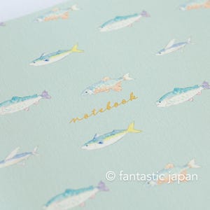 May include: A light blue notebook with a repeating pattern of watercolor fish in shades of blue, yellow, and orange. The word "notebook" is written in gold script. The copyright symbol and the words "fantastic japan" are at the bottom.