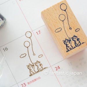 May include: A wooden stamp with two cats holding balloons. The stamp is on a calendar page with the date 17 circled. The text on the calendar page says "23 勤労感謝の日".