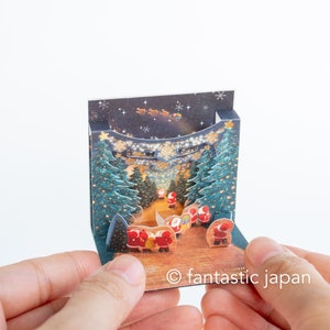 Pequeno cartão pop-up de Natal - mini mini Papais Noéis na iluminação da floresta -