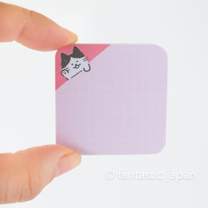May include: A pink and white square sticky note with a black and white cat illustration in the top corner. The note has a grid pattern.