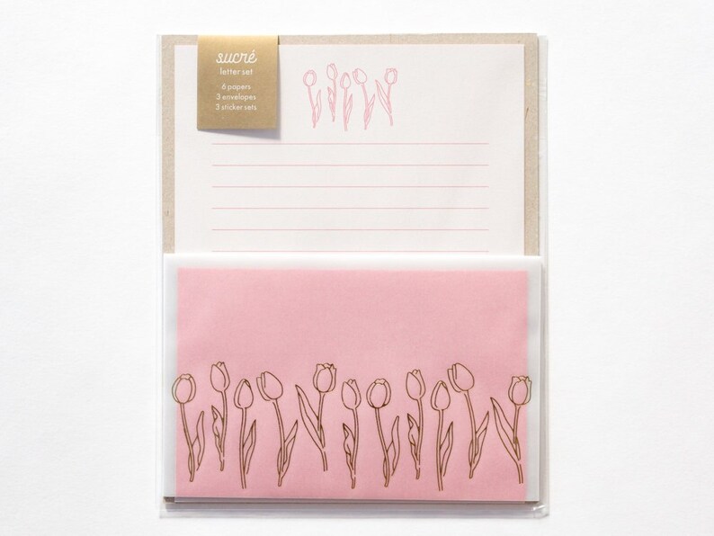 Puede incluir: Un juego de papeler&iacute;a rosa y blanca con un dise&ntilde;o de tulip&aacute;n dorado. El juego incluye 6 papeles, 3 sobres y 3 juegos de pegatinas. El texto en el paquete dice "sucr&eacute; letter set".