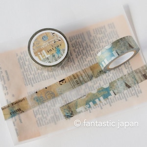 May include: Decorative washi tape rolls with vintage-style designs. The tape features a mix of text, stamps, and watercolor-like patterns in shades of blue, beige, and brown. The tape is displayed on a sheet of paper with printed text.