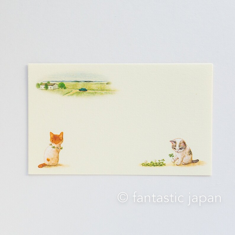 May include: A cream-colored stationery card featuring watercolor illustrations of two cats and a rural landscape. One cat is orange and white, the other is gray and white. The card has the text "fantastic japan" at the bottom.