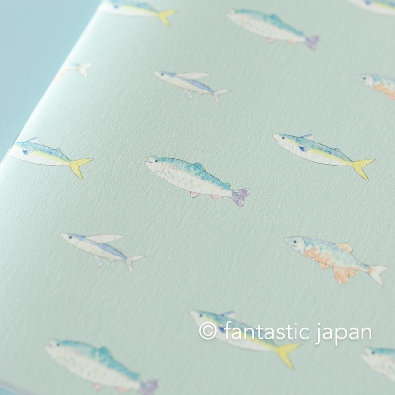 May include: A light blue notebook with a repeating pattern of watercolor fish in shades of blue, yellow, and purple. The text "fantastic japan" is in the lower right corner.