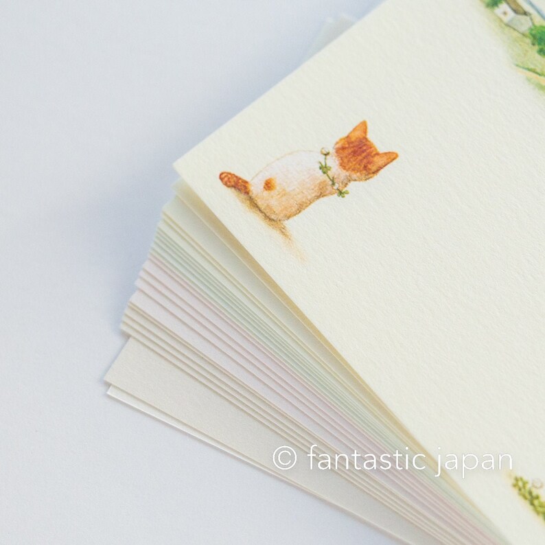 May include: A stack of stationery featuring a watercolor illustration of a ginger and white cat wearing a floral collar. The cat is lying down on a cream-colored paper. The bottom of the stack shows the edges of the paper with pastel colors. The text "fantastic japan" is in the bottom corner.