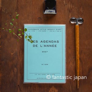 May include: A light blue paperback weekly diary for 2027 with the text PAPERBACK STYLE WEEKLY DIARY, NA-TYPE, 176 PAGES, 105 MM X 148 MM, LES AGENDAS DE L'ANNÉE, 2027, NO 004, LA VIE AVEC UN LIVRE, LES ÉDITIONS HIGHTIDE CO., LTD.