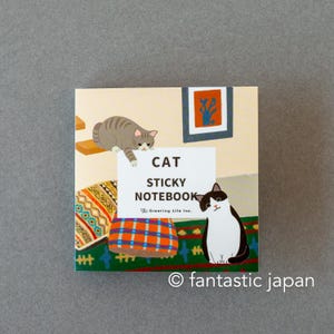 May include: A square sticky notebook with a cat theme. The cover features illustrations of cats, a framed artwork, and a patterned pillow. The text "CAT STICKY NOTEBOOK" is displayed prominently. The brand name "fantastic japan" is also visible.