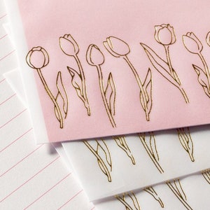 Puede incluir: Papeler&iacute;a rosa y blanca con dise&ntilde;os de tulipanes en pan de oro. Los tulipanes est&aacute;n delineados en oro y tienen un aspecto delicado y femenino.