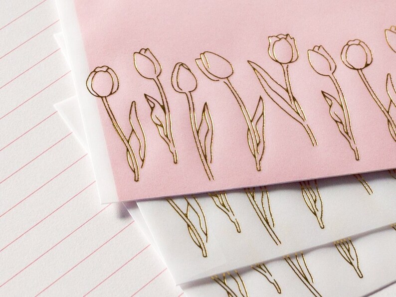 Puede incluir: Papeler&iacute;a rosa y blanca con dise&ntilde;os de tulipanes en pan de oro. Los tulipanes est&aacute;n delineados en oro y tienen un aspecto delicado y femenino.